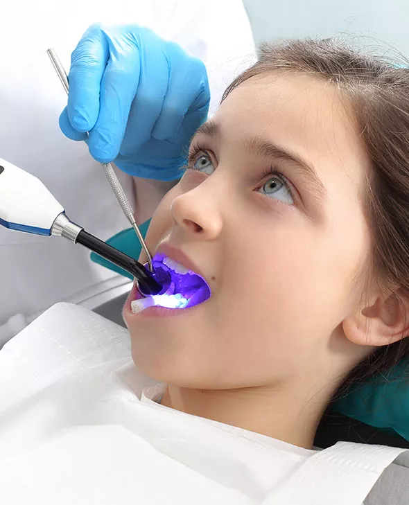 Young girl in operatory chair with dental tools in mouth.